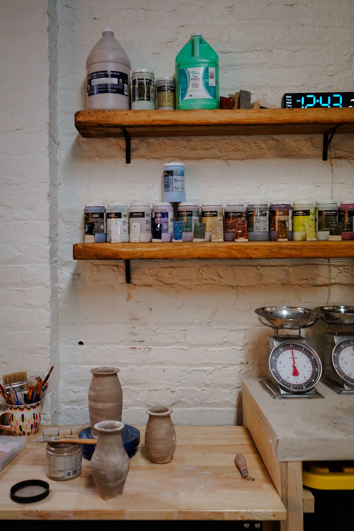 Wooden shelves of labeled Cone 6 studio glazes against whitewashed brick