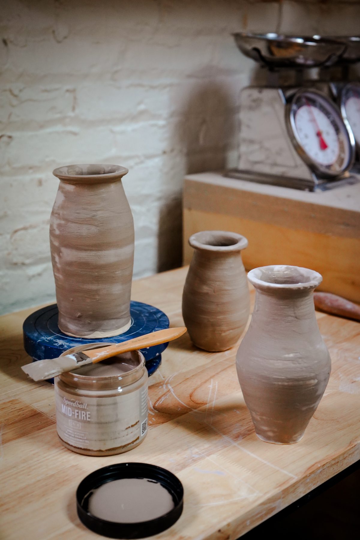 Freshly thrown greenware vases drying on a worktable beside a jar of underglaze